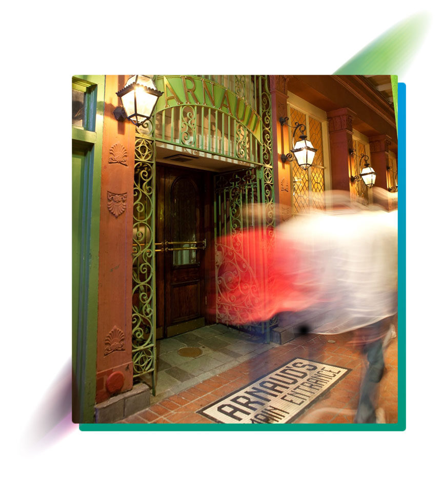 The main entrance of Arnaud's Restaurant in New Orleans with a vibrant, colorful facade and a blurred pedestrian passing by.