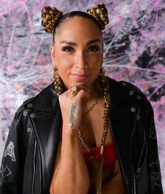 Robin Arzon's headshot: confident with intricate braids, black leather, gold jewelry, and a radiant smile against a pink and white background